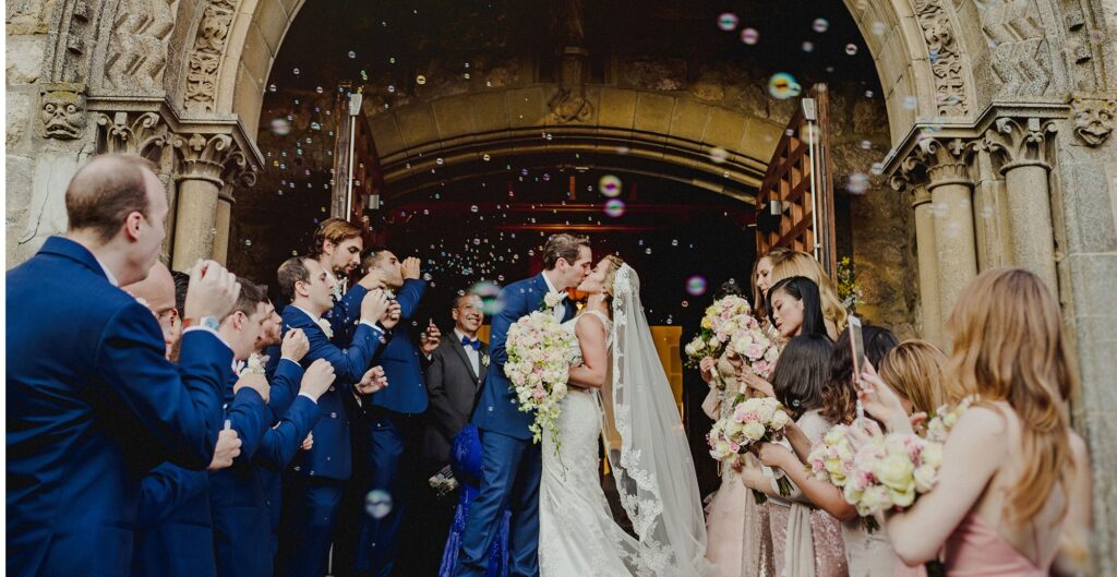Novios besandose en la entrada de la iglesia con burbujas flotando